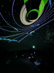 Photo of the inside of our portable planetarium, showing Saturn with it's rings, as well as it's shadow from the Sun and the orbit lines of the other planets in the solar system. The planetarium system and projector can also be seen in the dark at the bottom of the image.