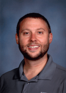McKay Thompson, Systems Specialist, is a smiling man with short brown hair and a beard. He is wearing a gray collared shirt.