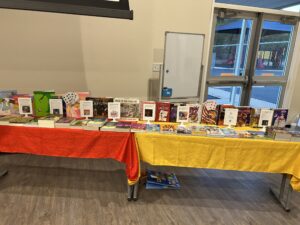 A long table covered with red and yellow tablecloths displaying many different books for children, likely at a book fair or resource table.